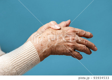 A senior woman is doing a brush massage, experiencing pain. Blue background, hands close-up. The concept of rheumatism and arthritis 93934533