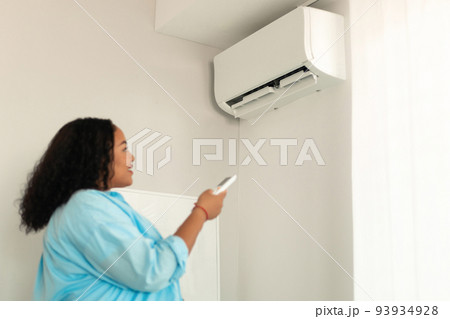 African Female Pointing Remote Controller Turning On Air Conditioner Indoor 93934928