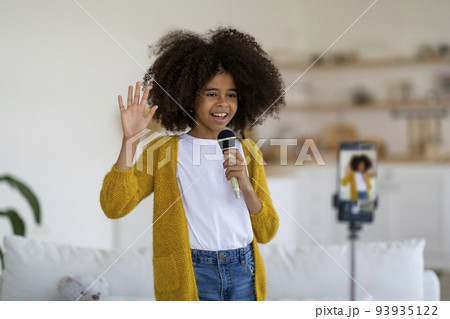 Cheerful black girl singing and recording video on mobile phone 93935122