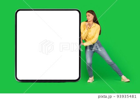Woman Pushing Big Square Empty Gadget Screen Over Green Background 93935481