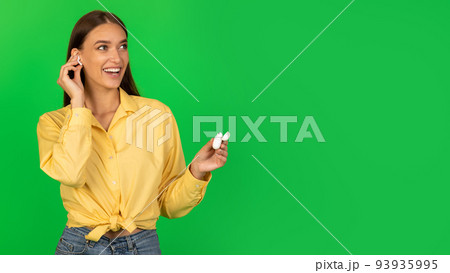 Cheerful Lady Listening To Music Via Earbuds Over Green Background Cheerful Lady Listening To Music Via Earbuds Over Green Background 93935995