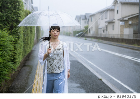 雨の中を傘をさして歩く女性 93940379