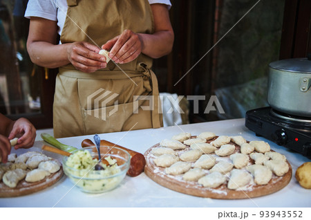 Cropped view of housewife, cook in beige chef's apron, making dumplings with potatoes. Ukrainian national dish Vareniki 93943552