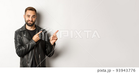 Skeptical and doubtful guy in black leather jacket, shrugging while pointing at upper right corner promo offer, standing over white background Skeptical and doubtful guy in black leather jacket, shrugging while pointing at upper right corner promo offer, standing over white background 93943776