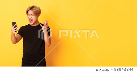 Portrait of angry and pissed-off asian man looking mad at smartphone screen, having argument during video call, standing yellow background Portrait of angry and pissed-off asian man looking mad at smartphone screen, having argument during video call, standing yellow background 93943844