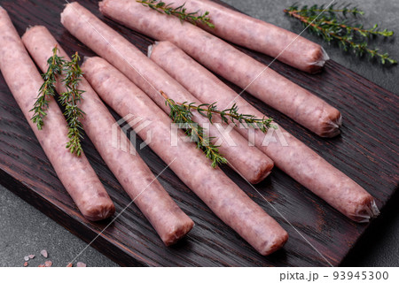 Raw sausages with spices on a wooden cutting board on a stone background with copy space for your text Raw sausages with spices on a wooden cutting board on a stone background with copy space for your text 93945300