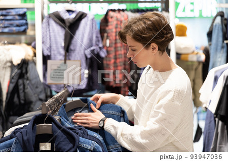 young woman chooses clothes in second hand young woman chooses clothes in second hand 93947036