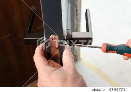 A man installs a doorknob in a door, carpentry at home. 93947714