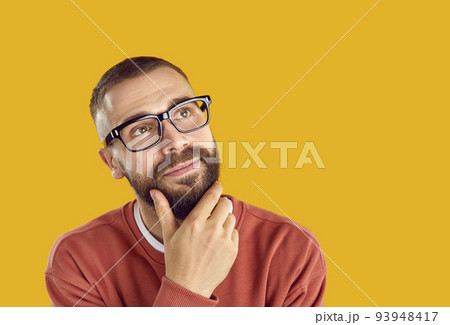 Young man in eyeglasses looking away at yellow copy space background and thinking 93948417
