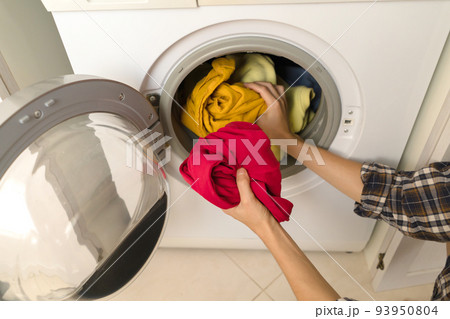 Woman puts bright clothes into a washing machine. 93950804