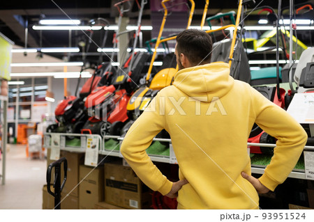 young gardener purchases a lawn mower in a gardening equipment store 93951524