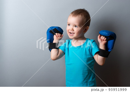 a little boy in boxing gloves and a blue T-shirt on a gray background.expression of emotions.copy space. 93951999