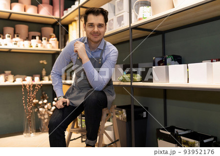 male florist in a flower shop surrounded by gift boxes and packages for flower arrangements male florist in a flower shop surrounded by gift boxes and packages for flower arrangements 93952176