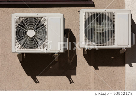 two units of outdoor air conditioners for heat dissipation are hung on the wall outside the building 93952178