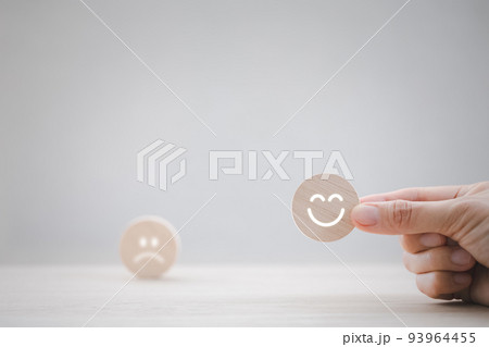 closeup businesswoman hand picking happy emotion face on wooden piece arranged on table for satisfaction survey 93964455