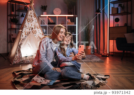 Beautiful cute sisters or friends sitting outside wigwam with smartphone. 93971342