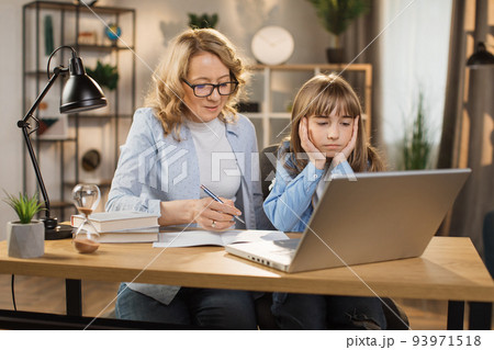 Caucasian tutor engaged with schoolgirl help complete tasks sitting at table at home. 93971518