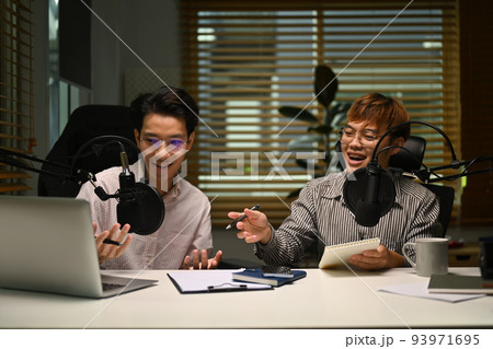 Two happy man using laptop and microphone streaming audio podcast at home studio. Entertainment, podcasts and technology concept 93971695
