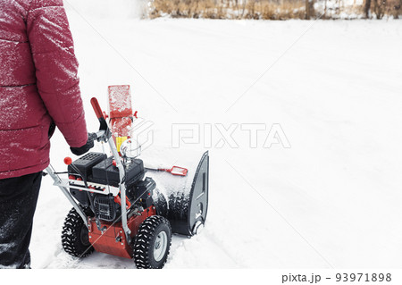 Detail of portable red snow blower powered by gasoline in action. Man outdoor using snowblower machine after snowstorm. Snow removal, thrower assistant in winter. Guy blowing snow during blizzard 93971898