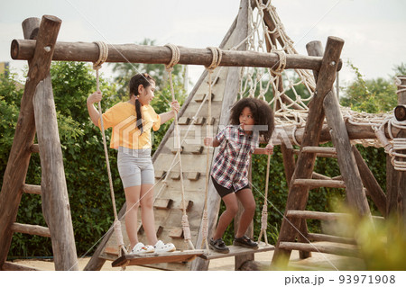 Two kids girl are playing on the swing in the outdoor playground. Two kids girl are playing on the swing in the outdoor playground. 93971908