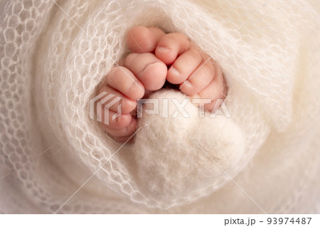 Knitted white heart in the legs of a baby. Soft feet of a new born in a white wool blanket. Close-up of toes, heels and feet of a newborn. Macro photography the tiny foot of a newborn baby. 93974487