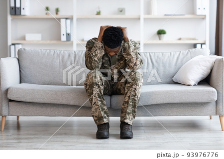 Stressed african american soldier in military uniform sitting on couch Stressed african american soldier in military uniform sitting on couch 93976776