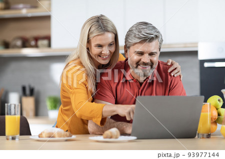 Loving couple enjoying healthy breakfast, using computer, kitchen interior Loving couple enjoying healthy breakfast, using computer, kitchen interior 93977144