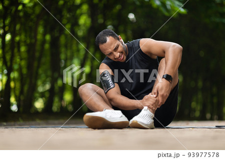 African american athlete in pain touching his ankle 93977578