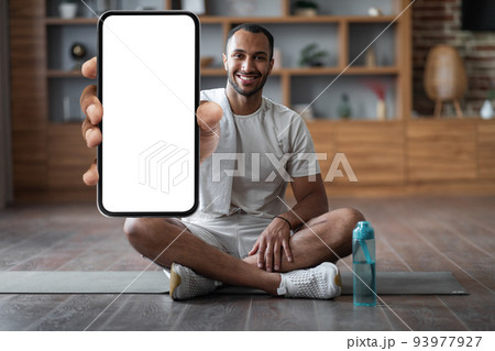 Fitness App. Happy Black Man Training At Home And Showing Blank Smartphone Fitness App. Happy Black Man Training At Home And Showing Blank Smartphone 93977927