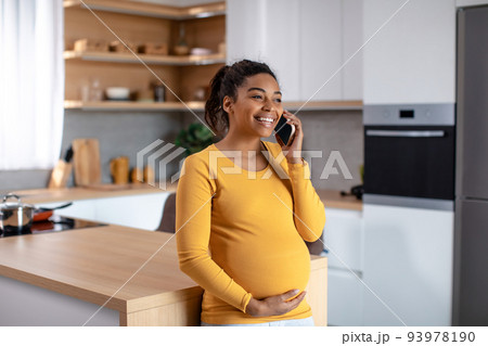 Happy pretty young pregnant african american woman touching belly and talking by phone Happy pretty young pregnant african american woman touching belly and talking by phone 93978190
