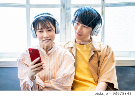 ヘッドホンでスマホ音楽を聴く若いカップル 93978343