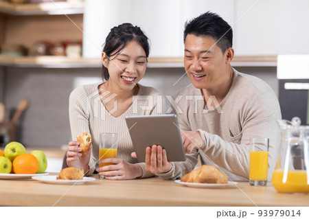 Smiling chinese spouses having breakfast and using tablet Smiling chinese spouses having breakfast and using tablet 93979014