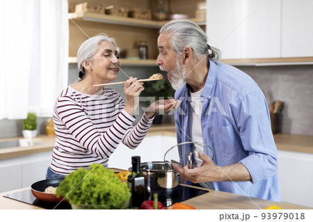Cheerful senior couple having fun while preparing lunch together in kitchen Cheerful senior couple having fun while preparing lunch together in kitchen 93979018