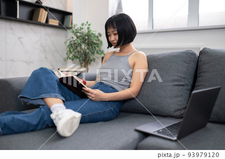 A short-haired young woman reading a book while sitting on the sofa A short-haired young woman reading a book while sitting on the sofa 93979120