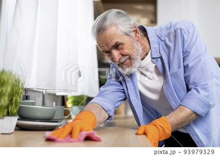 Portrait Of Smiling Elderly Man Washing Table In Kitchen With Rag 93979329