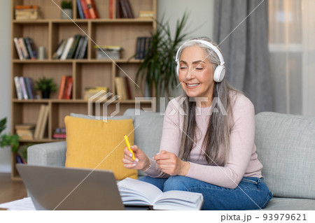 Cheerful caucasian mature gray-haired woman teacher in headphones speaks at laptop with student Cheerful caucasian mature gray-haired woman teacher in headphones speaks at laptop with student 93979621