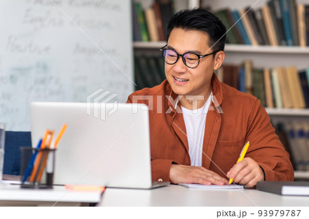 Japanese Male Tutor At Laptop Taking Notes Sitting At Workplace 93979787
