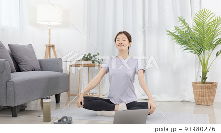 Beautiful Asian woman in sportswear is warming up or doing light exercises in the house with dumbbells and a protein shake or bottle of water and using a laptop at home, Healthy exercise. 93980276