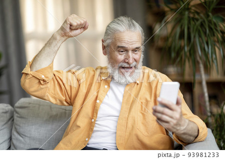 Excited grandfather gesturing while using mobile phone 93981233