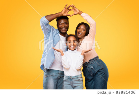 Excited black parents showing heart shape with fingers, making symbolic roof under their daughter head 93981406