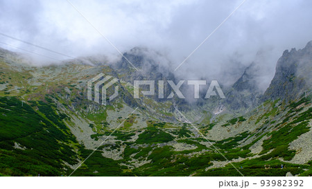 low hanging storm clouds and fog in the mountains on a summer day. blue haze in mountain valleys. 93982392
