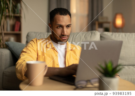 Serious millennial black male using laptop pc at home office Serious millennial black male using laptop pc at home office 93983195