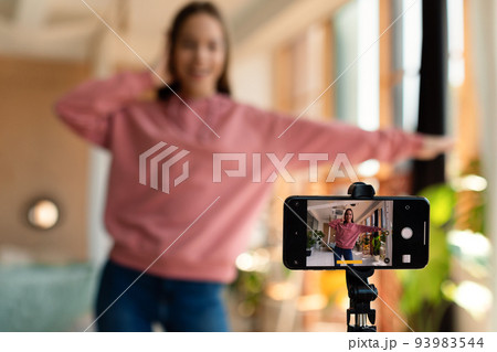 Modern teenage female influencer recording video on smartphone, dancing on camera at home, selective focus 93983544