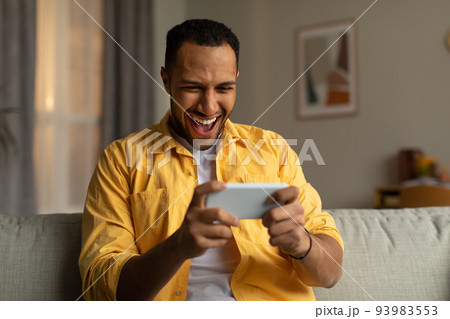 Overjoyed young black man with smartphone feeling excited over winning lottery or casino bet online at home 93983553