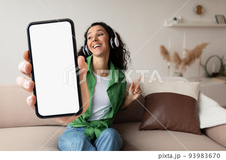 Music App. Cheerful Young Woman In Wireless Headphones Holding Big Blank Smartphone 93983670