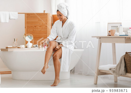 Pretty Woman Shaving Legs Using Safety Razor Sitting In Bathroom 93983671