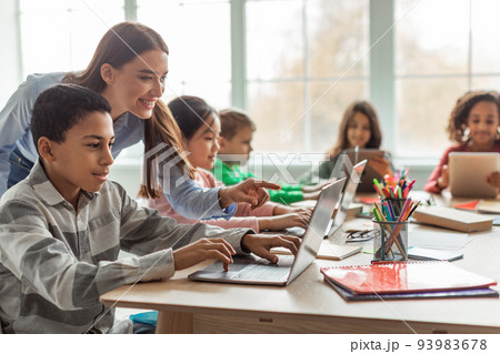 Teacher Teaching Diverse School Kids Using Laptop In Classroom 93983678