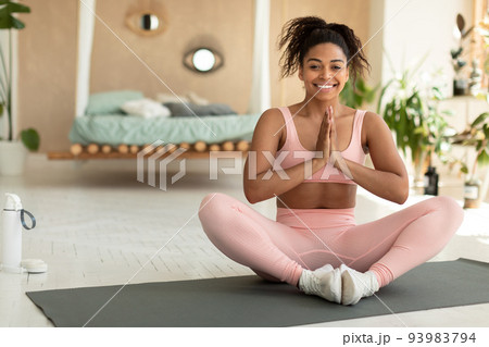 Morning yoga concept. Happy black lady practicing meditation in lotus position, sitting with clasped hands and smiling 93983794