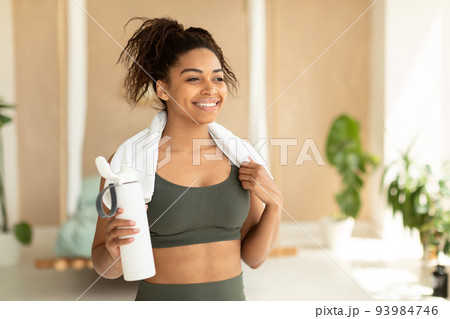 Portrait of happy black woman in sportswear and white towel on neck holding bottle with fresh water, copy space 93984746