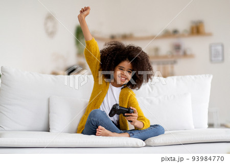 Cheerful little african american kid girl playing video game Cheerful little african american kid girl playing video game 93984770